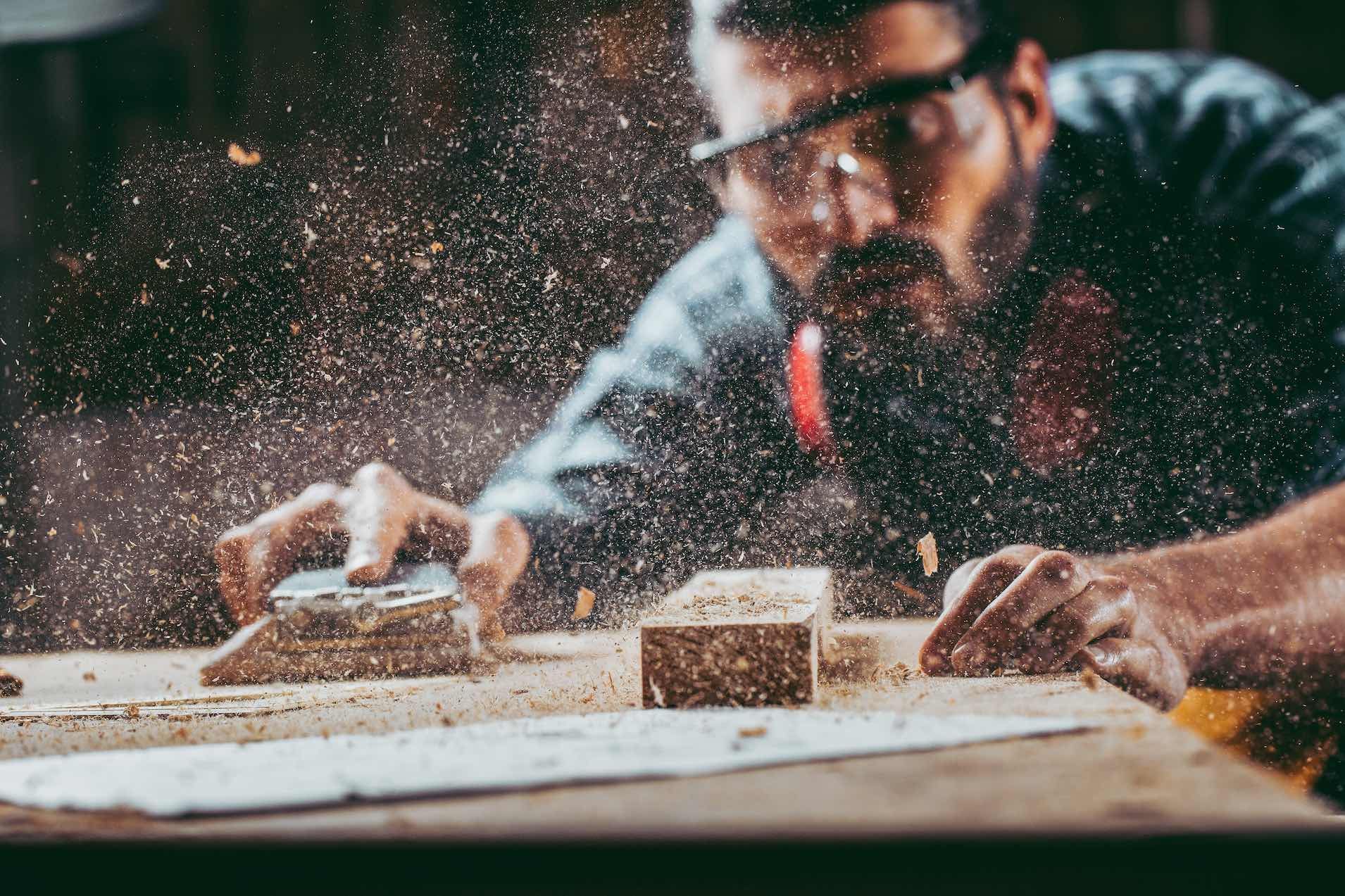 Man wearing goggles working in a wood shop sanding.